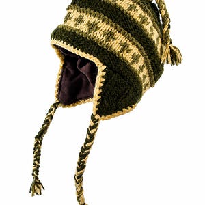May include: A dark green and cream-colored knit earflap hat featuring a geometric pattern, a solid dark brown interior lining, and two long braided tassels hanging from the sides. The hat is constructed with thick yarn and has a textured finish.