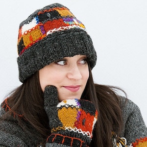 May include: A woman wearing a grey knitted hat with colourful patches and a matching pair of gloves. The hat and gloves have a patchwork design with various colours, including red, orange, yellow, green, blue, and purple.