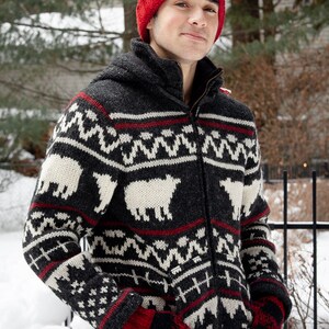 May include: A black and white patterned sweater with a red and black knit hat. The sweater features a zipper closure and a hood.