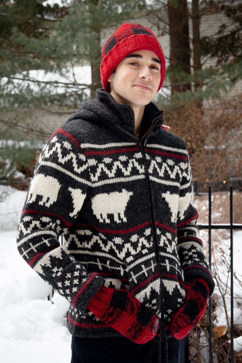 May include: A black and white patterned sweater with a red and black knit hat. The sweater features a zipper closure and a hood.