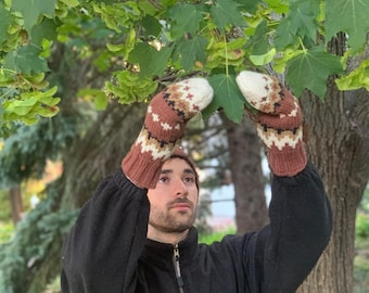 May include: A person wearing a black fleece jacket with a green logo, holding up a pair of brown and white knitted mittens with a geometric pattern.