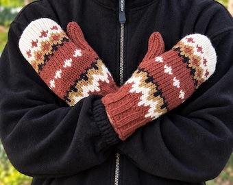 Puede incluir: Un par de manoplas de punto con un patrón geométrico en tonos naranja óxido, crema, negro y bronceado. Las manoplas tienen un puño acanalado y se usan sobre una chaqueta polar negra con cremallera y un tirador con la palabra BOLDIARY.