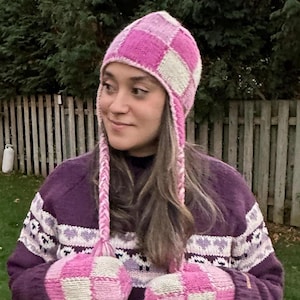 May include: A pink and white checkered knit hat with ear flaps and matching mittens. The hat and mittens are made of a soft, fuzzy yarn.