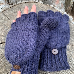 May include: A pair of dark blue fingerless gloves with a fold-over mitten flap. The gloves have a brown button on each flap and a brown leather tag with the word "AUTRY" on one glove.