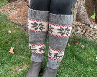 May include: Grey knitted leg warmers with a white and red snowflake pattern and a brown reindeer design. The leg warmers are worn over grey boots.