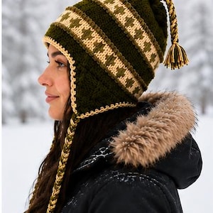 May include: A dark olive green crochet hat with earflaps, featuring a cream and green geometric patterned band. The hat includes braided side ties with tassels and a braided top accent with a matching tassel, all crafted in a textured knit.