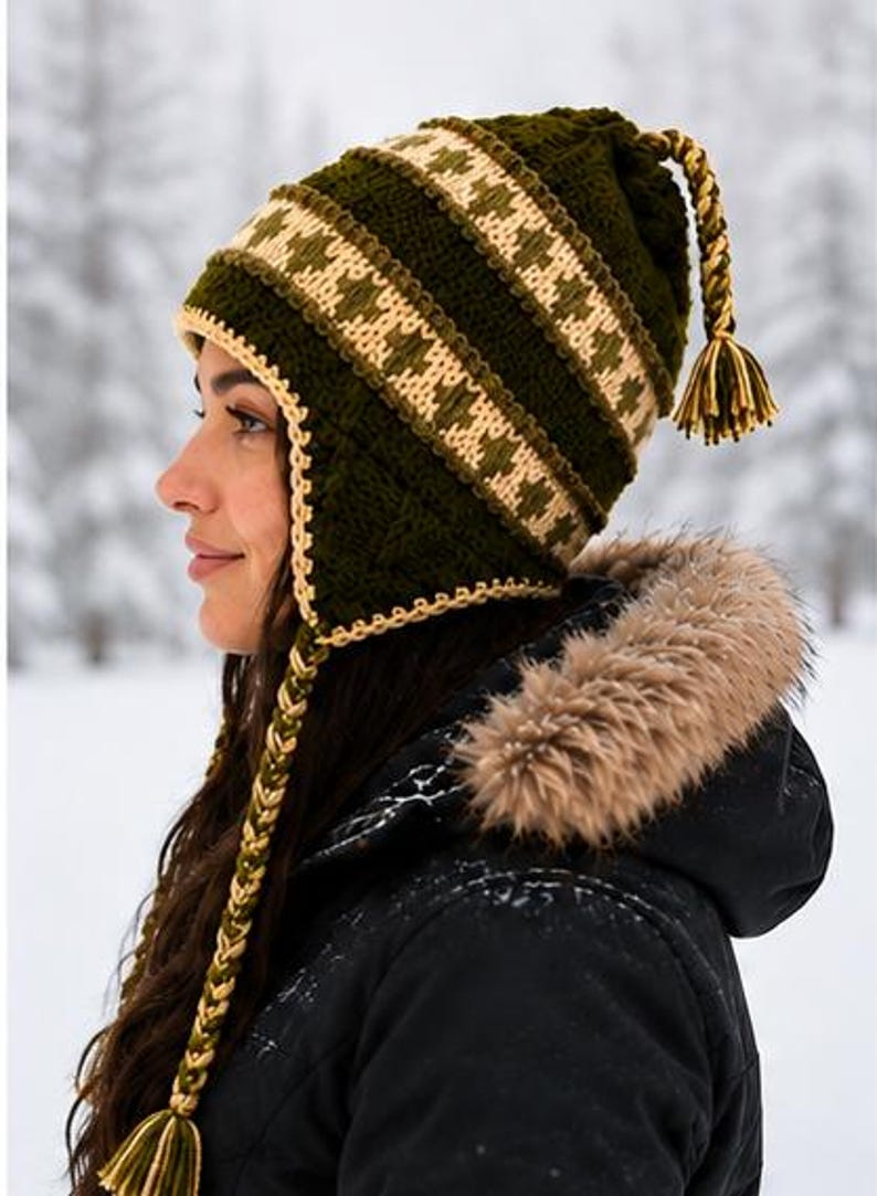 May include: A dark olive green crochet hat with earflaps, featuring a cream and green geometric patterned band. The hat includes braided side ties with tassels and a braided top accent with a matching tassel, all crafted in a textured knit.