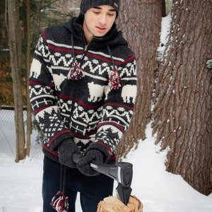 May include: A person wearing a black and white patterned sweater and a black beanie hat is chopping wood with a black axe. The person is standing in a snowy forest setting.