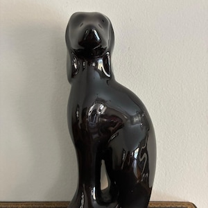 May include: A glossy black ceramic sculpture of a stylized dog. The figurine has a smooth, reflective surface and a sleek, modern design. The dog is depicted in a seated position with its head held high, showcasing a minimalist aesthetic.