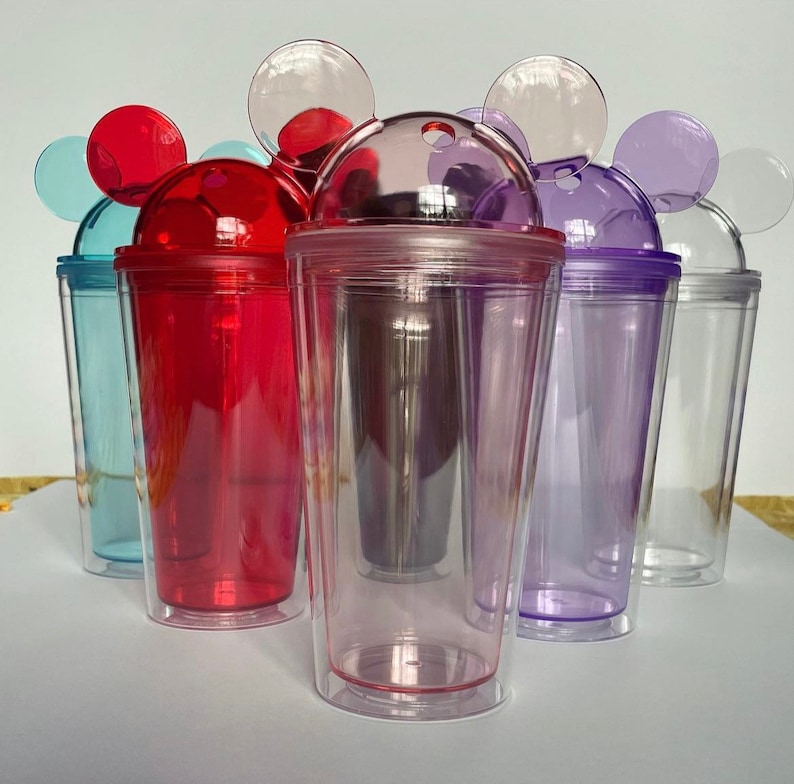 Puede incluir: Conjunto de seis vasos de pl&aacute;stico transparente con tapas de colores y orejas de Mickey Mouse. Los vasos son transparentes y tienen un agujero para pajita en la tapa. Las tapas son rojas, azules, moradas, rosas y transparentes.