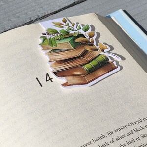 Könnte beinhalten: Ein Stapel antiker Bücher mit grünen Rücken und braunen Einbänden, verziert mit grünen Blättern auf weißem Hintergrund. Das Lesezeichen ist ein Aufkleber mit weißem Rand.