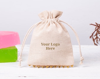 May include: A white cotton drawstring bag with gold beads around the top. The bag has the text "Your Logo Here" printed on the front.