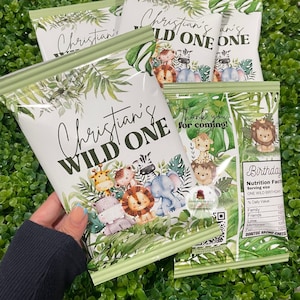 May include: Green and white party favor bags with a jungle theme. The bags feature a cartoon lion, zebra, giraffe, elephant, and hippo. The text on the bag reads "Christian's Wild One".