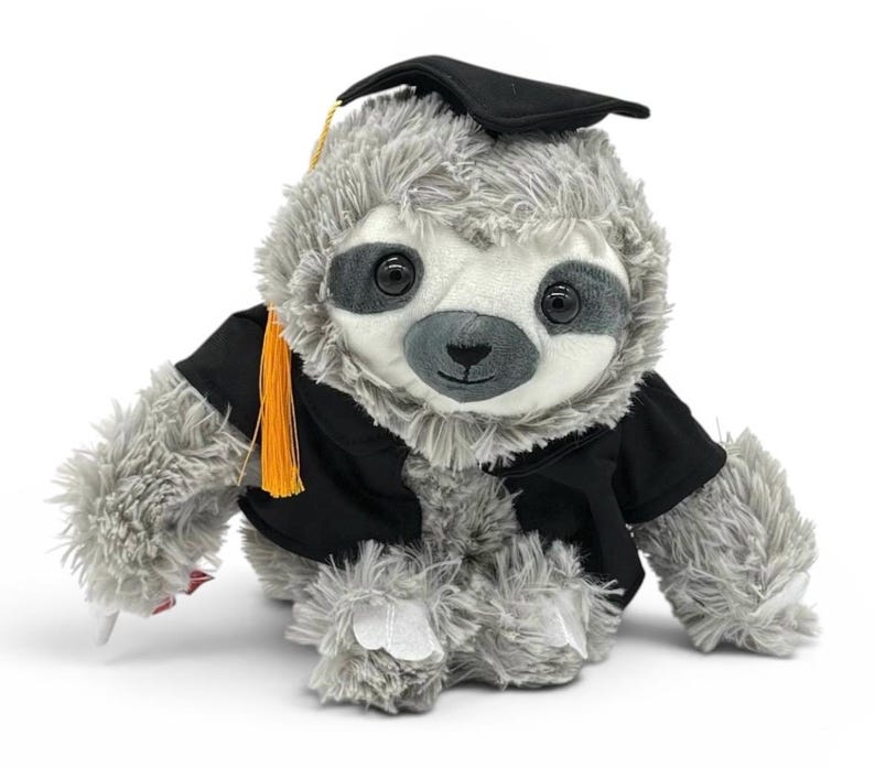 May include: A plush gray sloth wearing a black graduation cap and gown with an orange tassel. The sloth has a white face, large black eyes, and a small black nose. The plush toy is designed to look like a graduate.