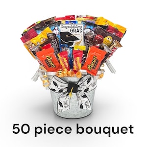 May include: A candy bouquet in a galvanized metal bucket, featuring a variety of wrapped candies and a graduation-themed card. The bucket is adorned with a graduation cap bow and ribbon. The text "50 piece bouquet" is at the bottom.