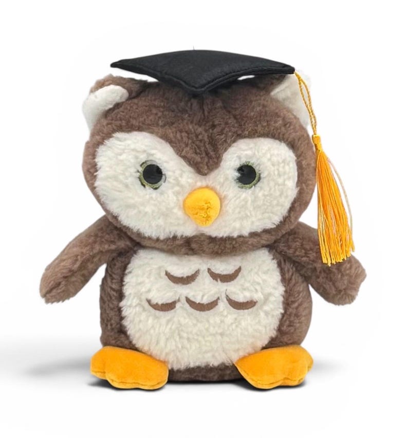 May include: A plush owl toy with brown and white fur, wearing a black graduation cap with a gold tassel. The owl has large, round eyes and orange feet. A cute graduation gift.