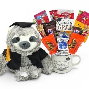 May include: A plush gray sloth wearing a graduation cap and gown sits next to a white mug filled with candy bars. The mug reads "Motivated, Educated & Graduated." A sign says "Congrats Grad."