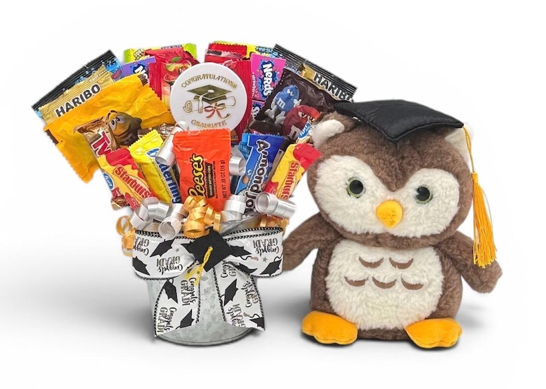 May include: A graduation gift basket with assorted candy and a plush owl wearing a graduation cap. The candy is arranged in a decorative bucket with a graduation-themed ribbon. A round sticker says "Congratulations Graduate".