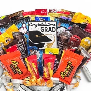 May include: A candy bouquet with a variety of wrapped candies, including Reese's, Starburst, and Hershey's. A card in the center reads "Congratulations Grad" with a graduation cap graphic. The arrangement is in a decorative container.
