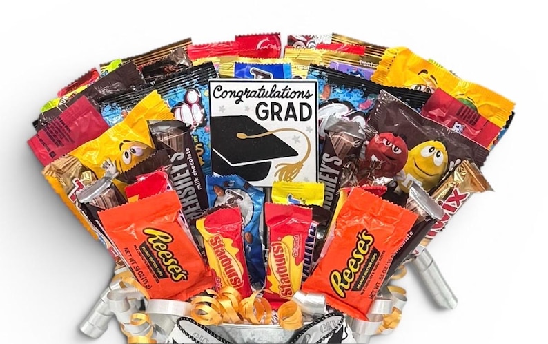 May include: A candy bouquet with a variety of wrapped candies, including Reese's, Starburst, and Hershey's. A card in the center reads "Congratulations Grad" with a graduation cap graphic. The arrangement is in a decorative container.