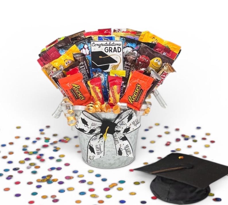 May include: A graduation-themed candy bouquet in a galvanized metal bucket, filled with various wrapped candies. The bucket is adorned with a graduation ribbon. A graduation cap and colorful confetti are scattered around the bucket.