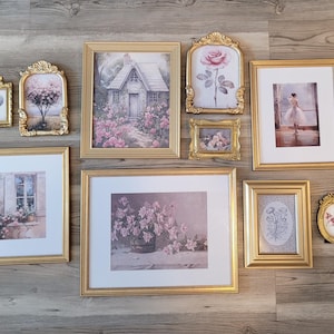 May include: An assortment of framed art pieces with gold frames. The artwork includes floral prints, a cottage scene, and a ballerina. The frames vary in size and shape, creating a gallery wall aesthetic.