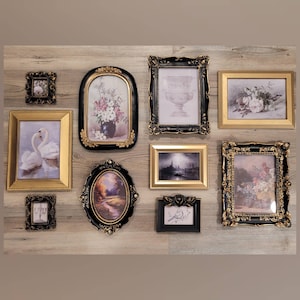 May include: A collection of ornate picture frames in various shapes and sizes, arranged on a light wood-grain surface. The frames feature gold and black detailing, with images of flowers, swans, and landscapes.