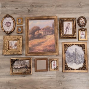 May include: A collection of framed art pieces in various sizes and shapes, arranged on a wooden surface. The frames are primarily gold-toned, with ornate detailing. The artwork includes landscape paintings, portraits, and decorative illustrations.