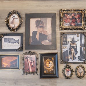 May include: A gallery wall arrangement featuring various framed art prints. The collection includes a ballerina, a person drinking wine, a whale, a witch reading, a sun and moon motif, and food illustrations, all encased in ornate black and gold frames.