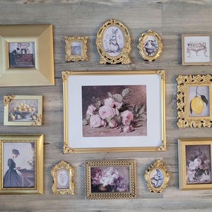 May include: A wall gallery featuring 11 gold picture frames with various images, including a floral still life, a lemon, a rabbit, and a woman in a vintage dress.