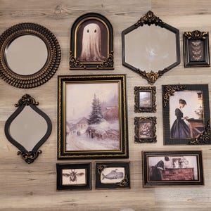 May include: A collection of decorative wall art, including mirrors and framed pictures. The mirrors have ornate frames in black and gold. The framed pictures feature a ghost, a winter landscape, and other vintage-style illustrations.