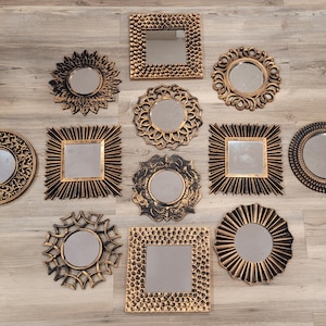 May include: An assortment of decorative wall mirrors in various shapes, including round, square, and floral designs. The mirrors have gold and black frames, creating a vintage or antique aesthetic. The arrangement showcases a variety of styles for home decor.