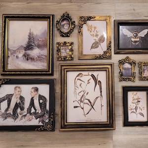 May include: A collection of framed art pieces with ornate black and gold frames. The artwork includes a winter landscape, botanical prints, a bee illustration, and portraits of people.