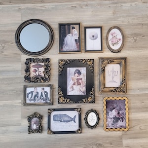May include: A collection of framed art and a round mirror arranged on a wooden surface. The frames vary in size, shape, and style, including ornate gold and black frames. The artwork includes portraits, floral prints, and a whale illustration.