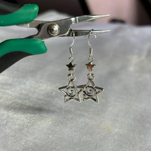 May include: Silver dangle earrings with a star design. The stars have a swirl pattern inside.