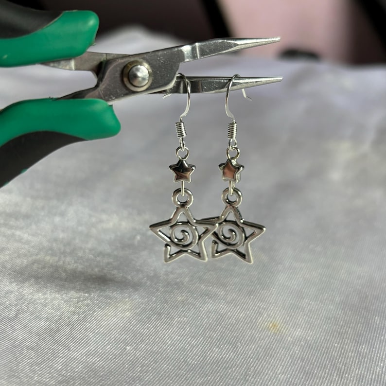 May include: Silver dangle earrings with a star design. The stars have a swirl pattern inside.