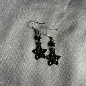 May include: A pair of silver earrings with black star-shaped charms. Each star has a swirl design in the center.