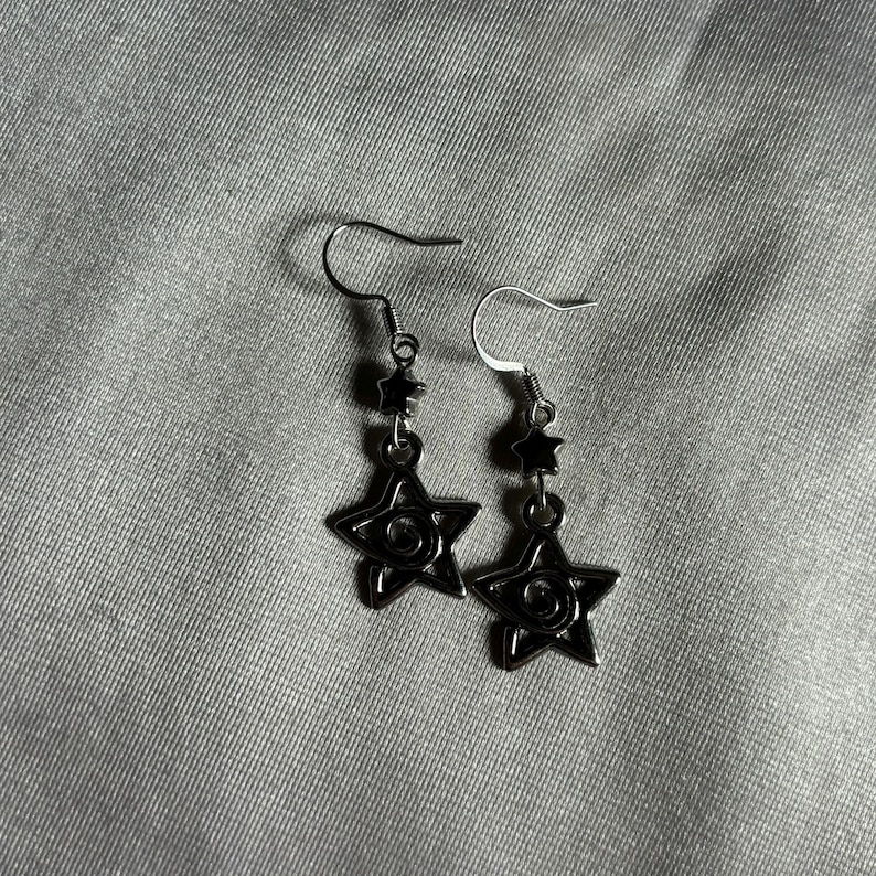 May include: A pair of silver earrings with black star-shaped charms. Each star has a swirl design in the center.