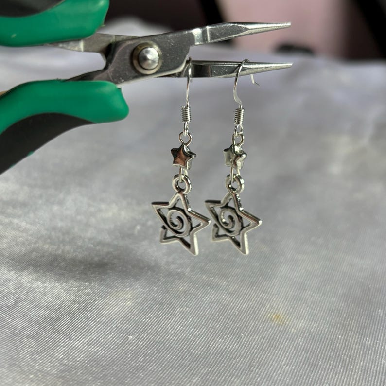 May include: Silver dangle earrings with a star and swirl design.