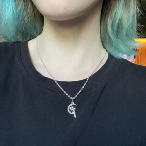 Puede incluir: Un collar de cadena de plata con un colgante que representa a un hada sentada en una luna creciente.