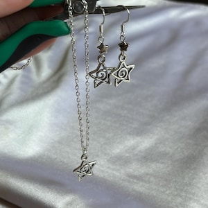 Op de afbeelding: Een zilveren ketting- en oorbellenset met een sterhanger met een swirl-ontwerp. De ketting heeft een delicate ketting en de oorbellen zijn van het hangende type.