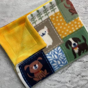 May include: A fleece pet bed with a yellow interior and a patchwork exterior. The patchwork features squares with images of dogs, cats, and floral patterns in various colors, including brown, white, blue, and green. The bed is designed for small pets.