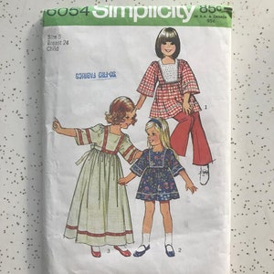 May include: Vintage Simplicity sewing pattern for children's dresses. The pattern is for sizes 5, with a 24-inch bust. The pattern includes three different dress styles, one with a red and white gingham print, one with a floral print, and one with a solid white fabric. The pattern is from the 1970s.
