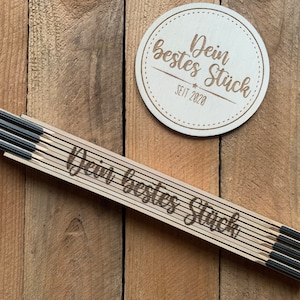 Könnte beinhalten: Ein Holz-Klapplineal mit dem eingravierten Text "Dein bestes Stück seit 2020". Das Lineal ist geschlossen und hat schwarze Metall-Akzente.