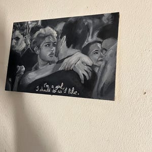 Puede incluir: Una pintura en blanco y negro de un grupo de personas. La mujer del centro mira al espectador y tiene los brazos alrededor de un hombre. El texto "I'm a girl I should do as I like." est&aacute; escrito en pintura blanca en la parte inferior de la pintura.