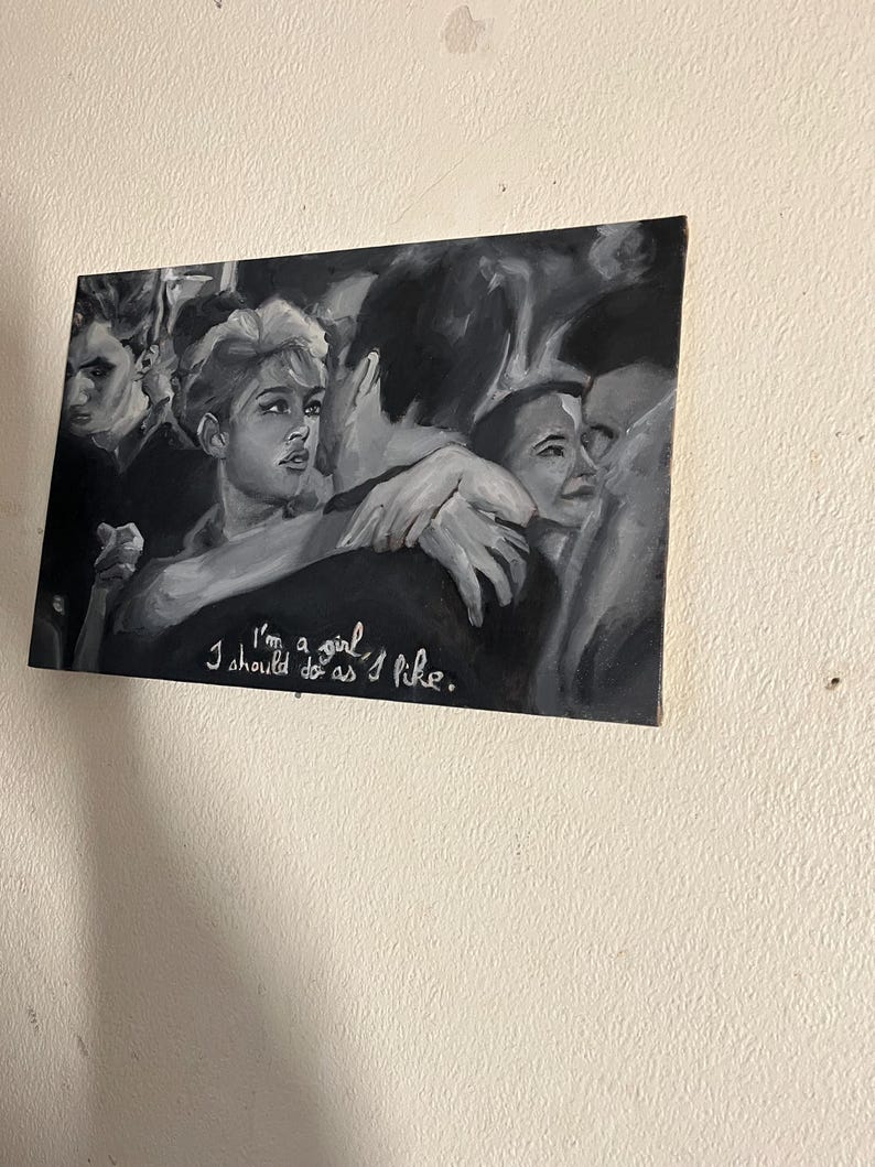 Puede incluir: Una pintura en blanco y negro de un grupo de personas. La mujer del centro mira al espectador y tiene los brazos alrededor de un hombre. El texto "I'm a girl I should do as I like." est&aacute; escrito en pintura blanca en la parte inferior de la pintura.