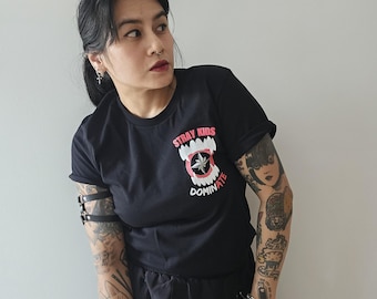 May include: Black t-shirt with a red and white graphic of a mouth with fangs and a marijuana leaf inside. The text "Stray Kids Dominate" is printed on the shirt.