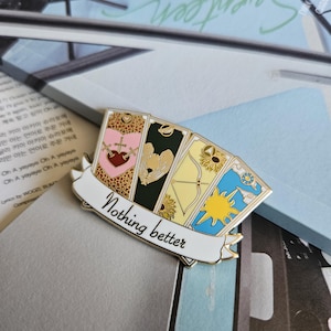May include: A gold-colored enamel pin with a white banner that reads "Nothing better". The pin features four cards with different designs, including a heart, an angel, an arrow, and a sunflower.