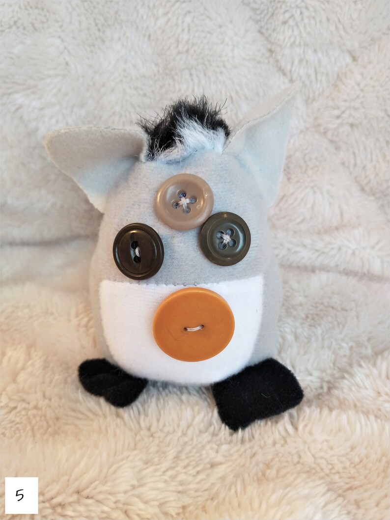 May include: A grey and white plush toy with black ears and a black tail. The toy has brown, orange and green button eyes.