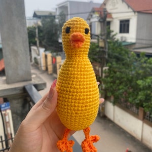 May include: A crocheted yellow duck toy with orange feet. The duck has black eyes and a bright orange beak.